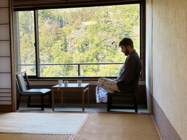 Best Ryokan in Kyoto: Which Type Actually Makes Sense for Your Trip? Foreign tourist wearing a yukata in a ryokan relaxing in his room in front of a window with view over the surrounding valley in Kyoto, Japan