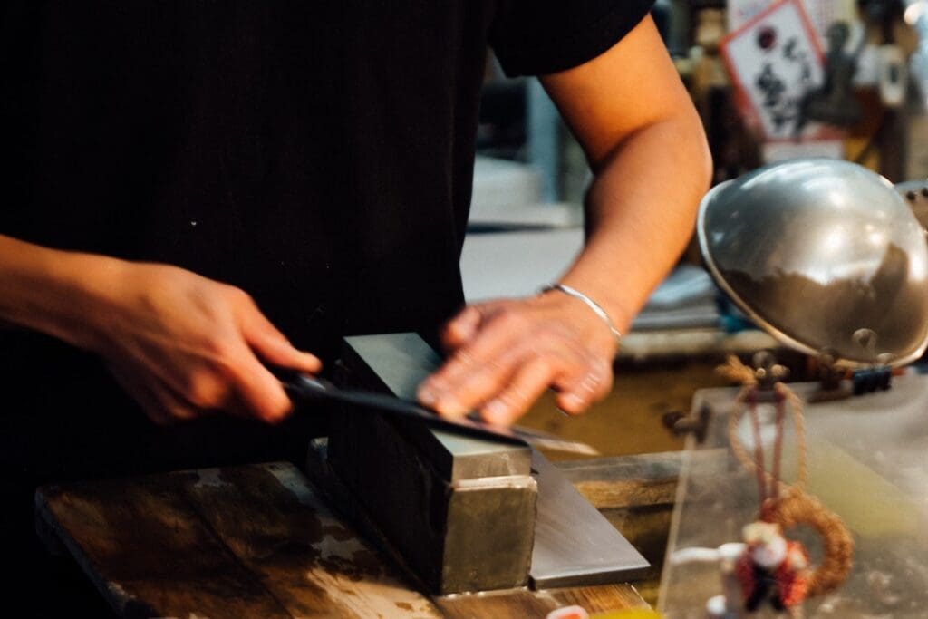 Hands of a man in a black t-shirt sharpening a Japanese knife on a sharpening stone