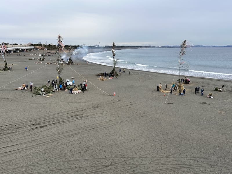 Sagicho Festival preparations on the beach in Oiso, with decorated structures and people gathered near the ocean.