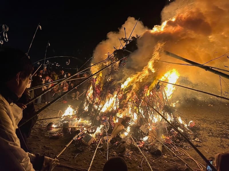 People roasting dango over the flames of the Sagicho Festival fire in Oiso at night.