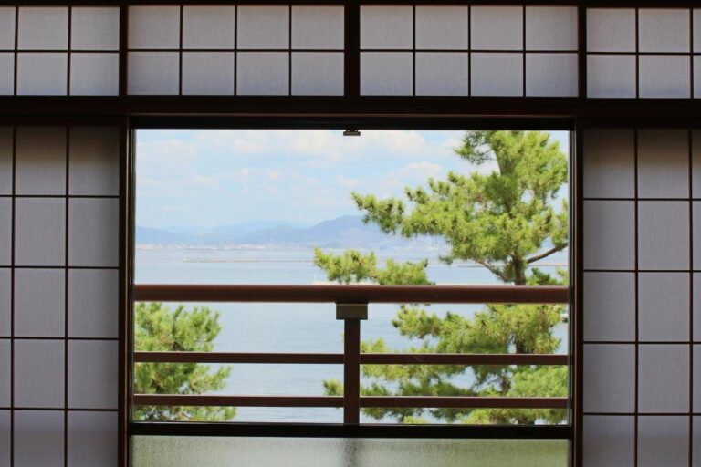 Best Ryokan in Miyajima: 6 Stays Worth Booking View of the ocean and pine trees seen through the window of a Japanese-style room at Miyajima Seaside Hotel.