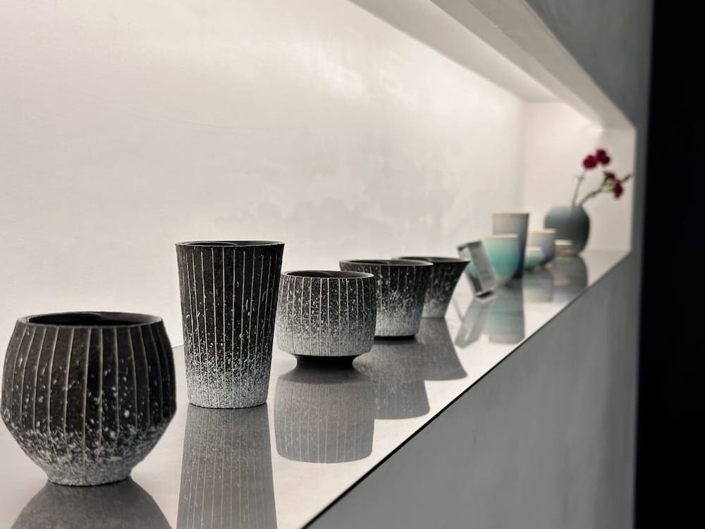 Row of handmade ochoko sake cups displayed on a recessed shelf at Hasegawa Eiga in Tokyo