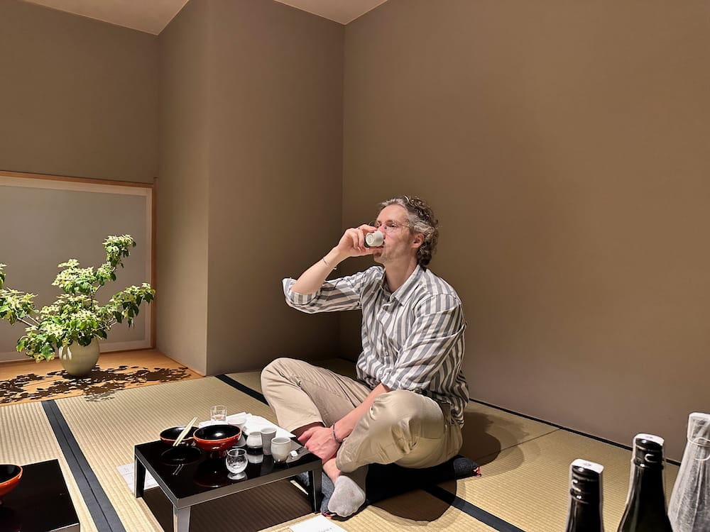 Person sitting on tatami floor drinking sake during the tasting session at Hasegawa Eiga.