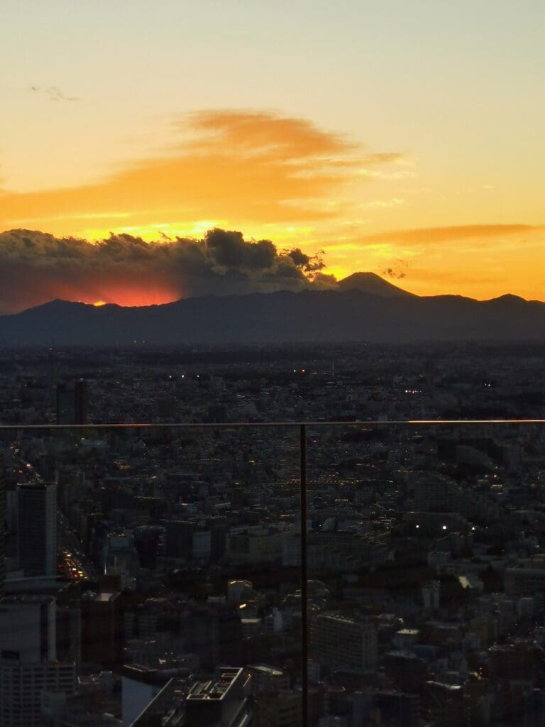 Aerial view of Shibuya cityscape at sunset with Mt Fuji silhouette under an orange sky