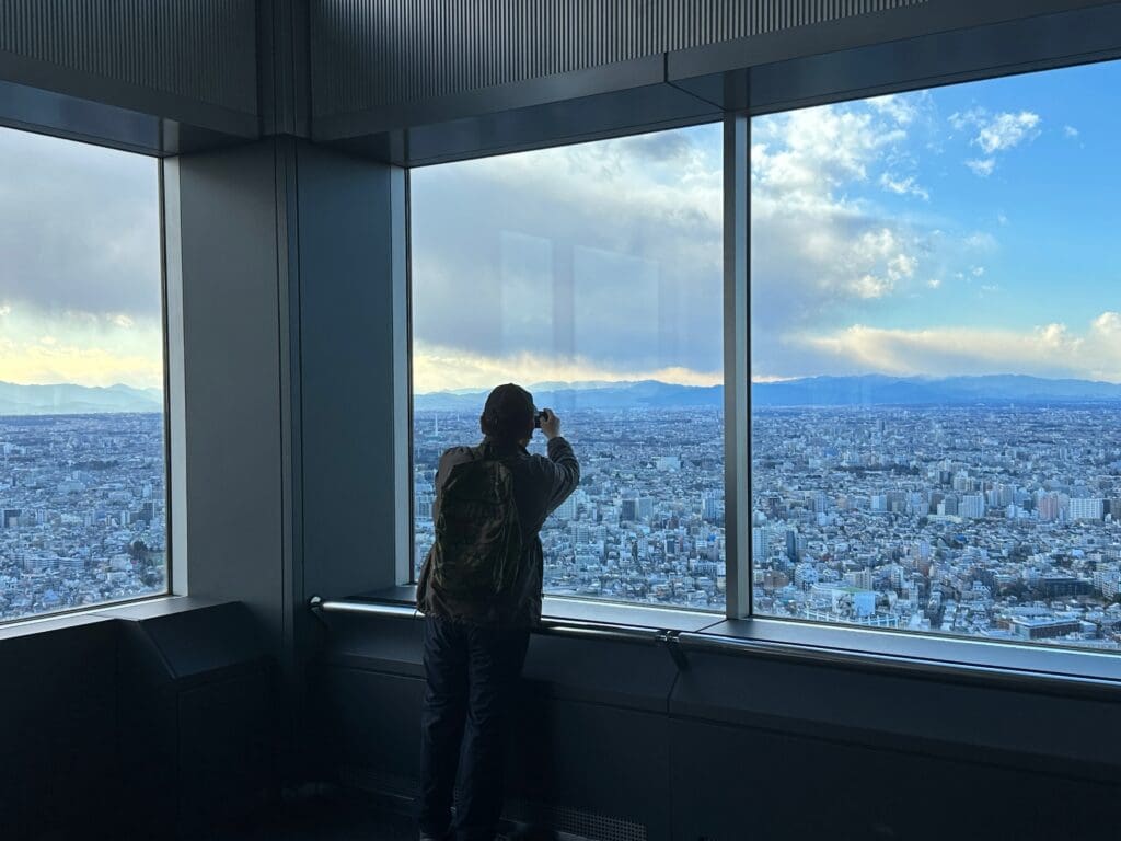 Person taking photo of Tokyo skyline through windows at the Tokyo Metropolitan Government Building observation deck