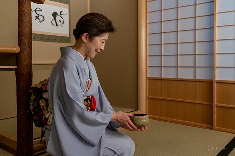 Woman in kimono serving tea in a tatami room with shoji screens at Towa Ryokan