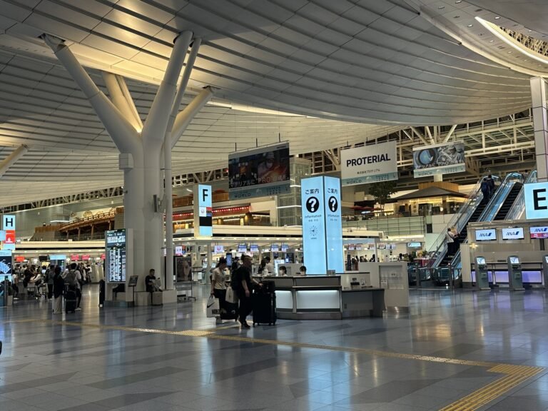 Haneda Airport departures hall with check-in counters, information booths, and travelers walking under a large white ceiling structure