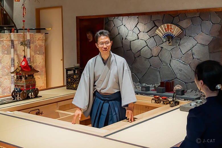 Man in a kimono standing behind a counter in a Kyoto art gallery or restaurant interior