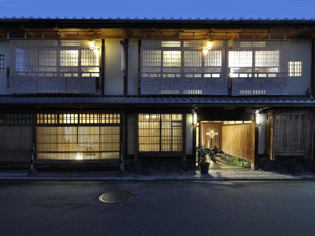 Exterior of Izuyasu, a traditional Kyoto ryokan, at dusk with warm lights glowing behind wooden lattice windows