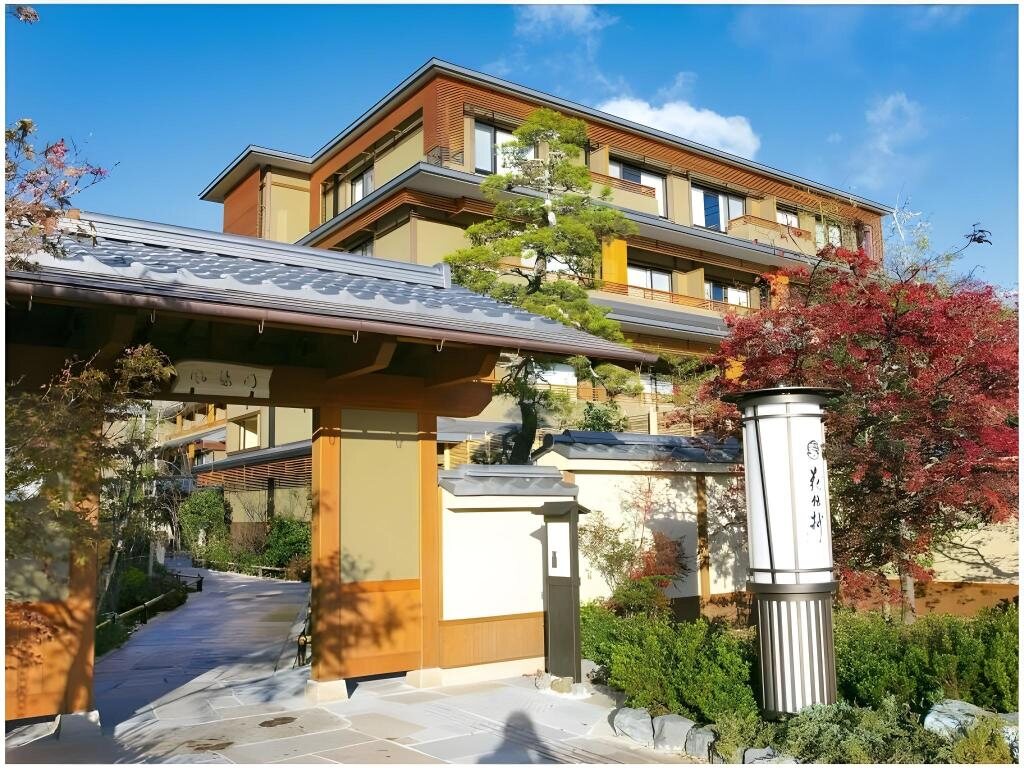 Entrance to Kadensho ryokan in Arashiyama, Kyoto, with autumn trees and a multi-story hotel building behind it