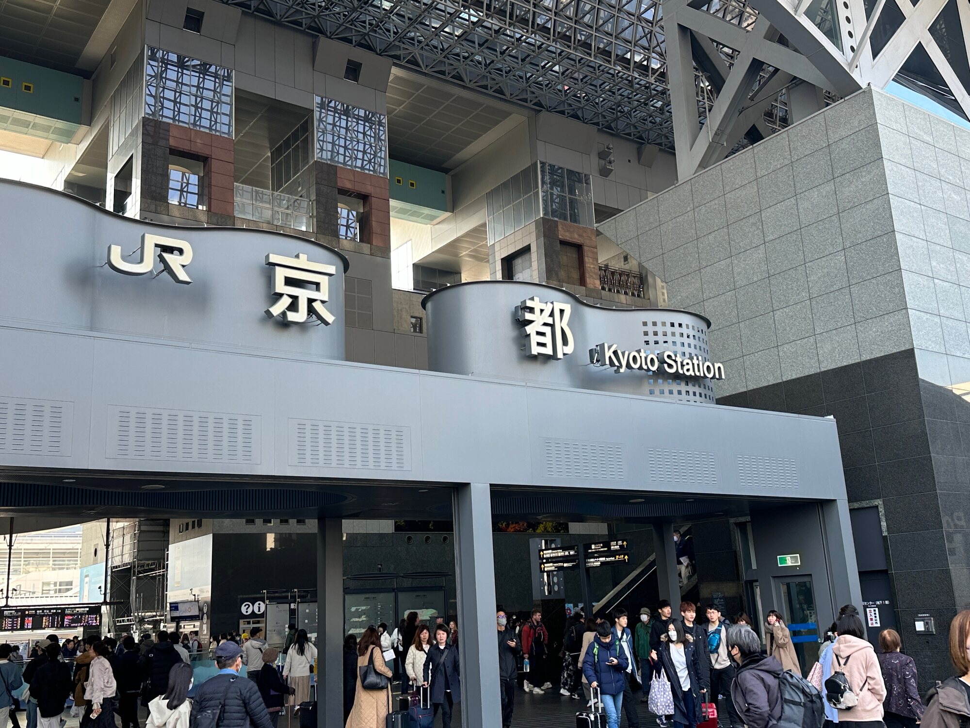 JR Kyoto Station entrance with large JR and 京都 signs and a crowd of travelers in the foreground