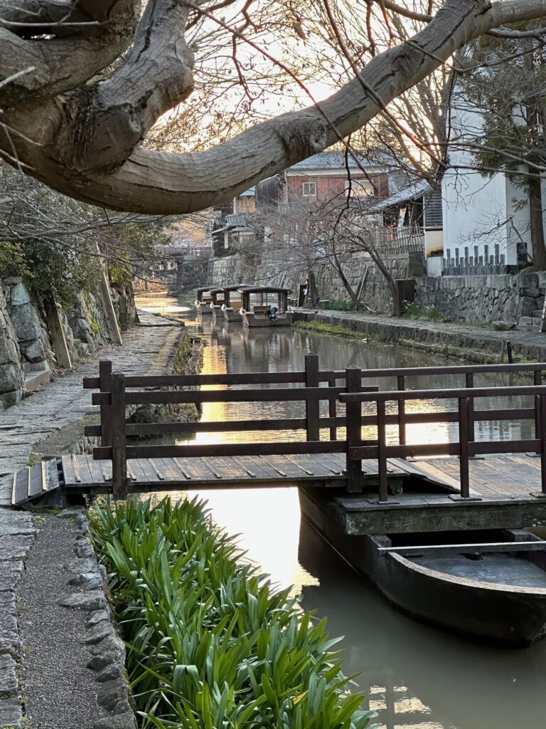 Canal walkway at the Omihachiman Canal Bridge area with a narrow water channel, small boats, and stone walls under bare winter trees