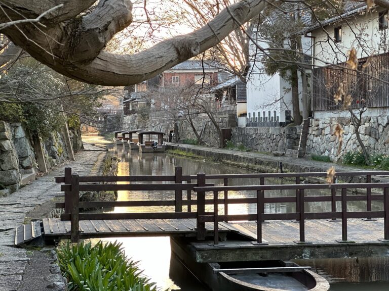 Japan Golden Route: Should You Follow It or Go Beyond It? View of the Omihachiman canal bridge area with a stone-lined canal, a wooden walkway, and small boat docks under leafless trees