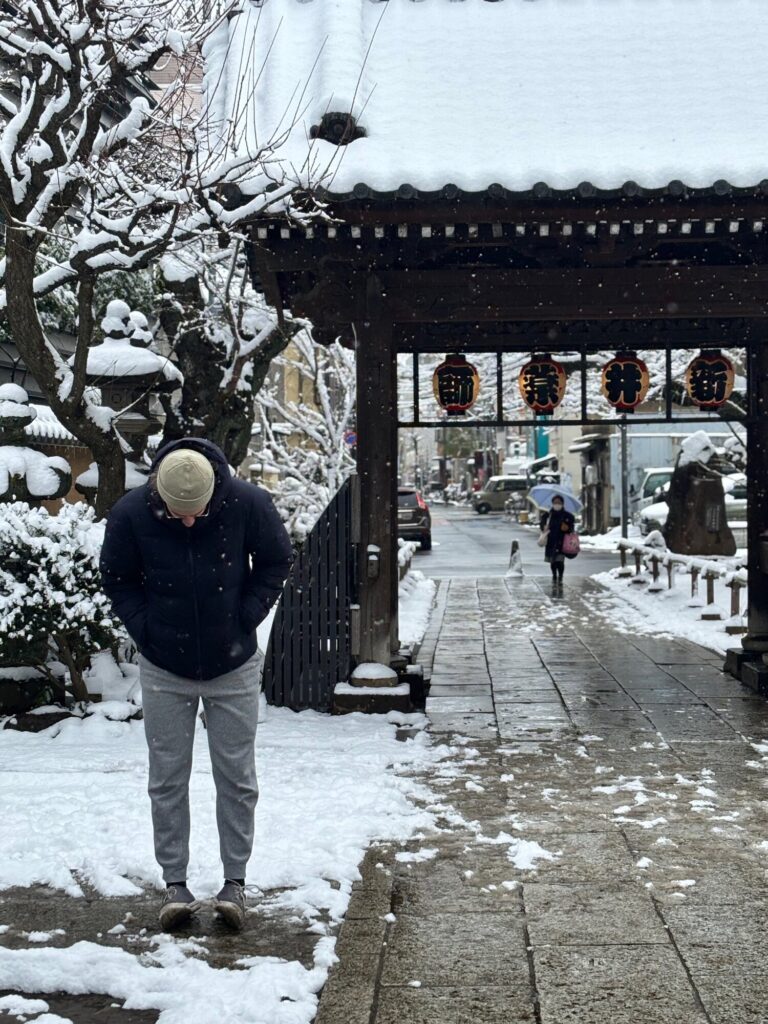 Person standing in the snow at the entrance gate of Arai Yakushi temple in Tokyo