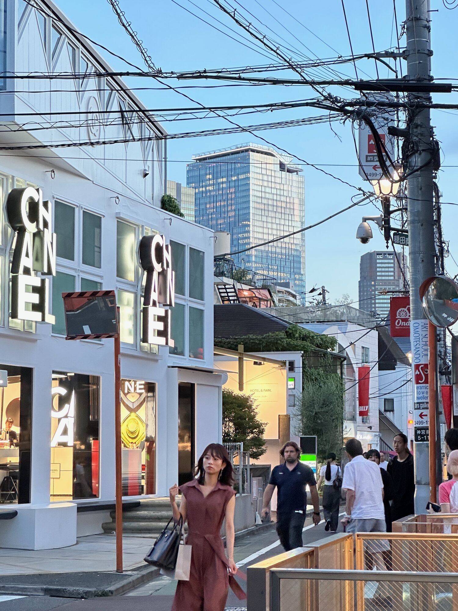 Pedestrians on a Shibuya street in Tokyo near a Chanel storefront and overhead utility wires