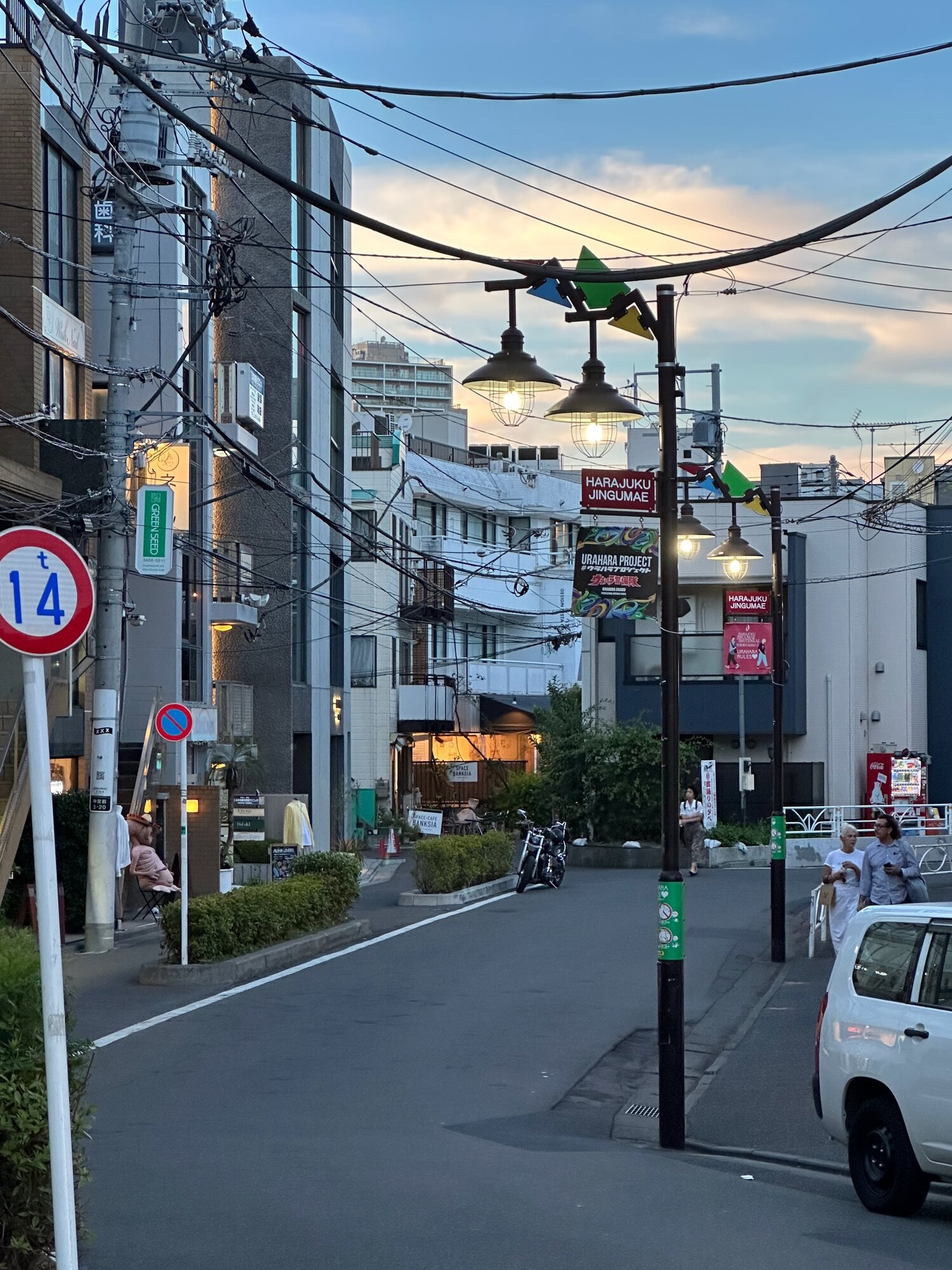 Harajuku Jingumae street in Tokyo at sunset with overhead wires, lit street lamps, and low-rise buildings
