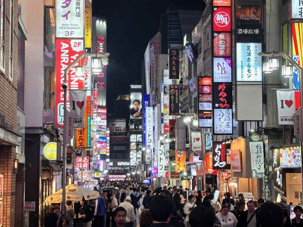 Crowded night street in Tokyo's Shinjuku district with bright restaurant and bar signs